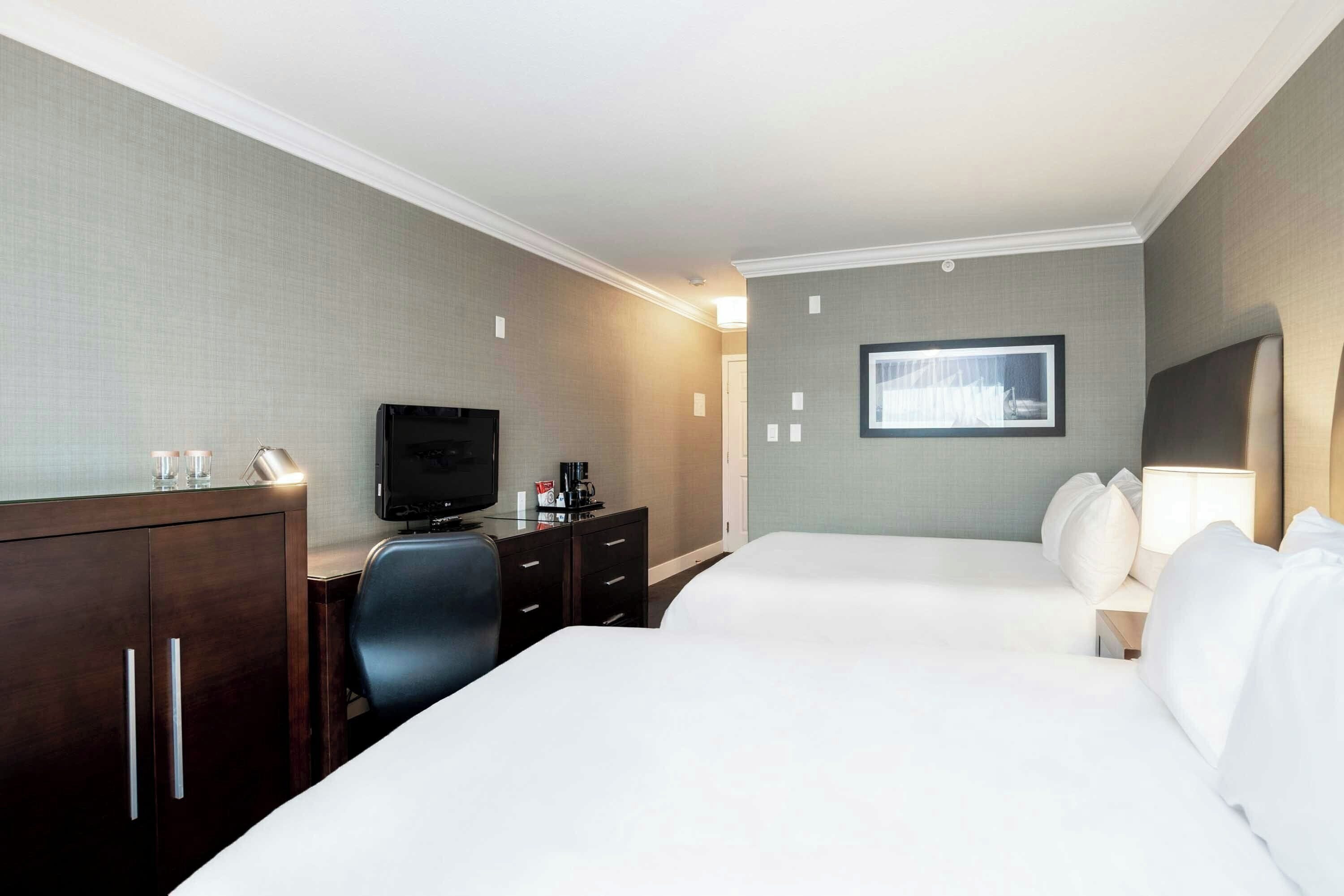 A hotel room with a bed, a desk with a television, a chair, and a dresser.