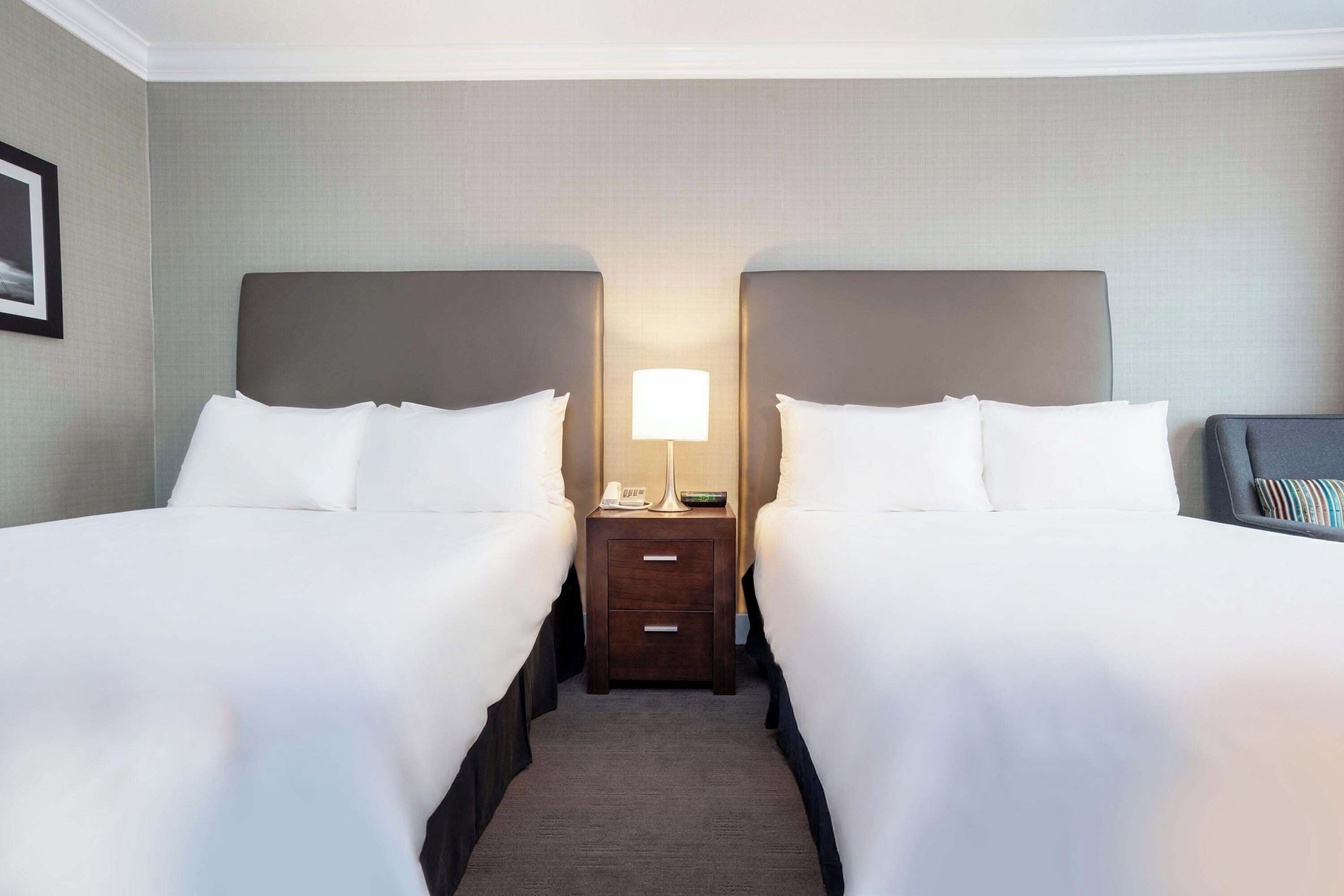 Une chambre d’hôtel avec deux lits, une table de chevet avec une lampe et un tableau encadré au mur.