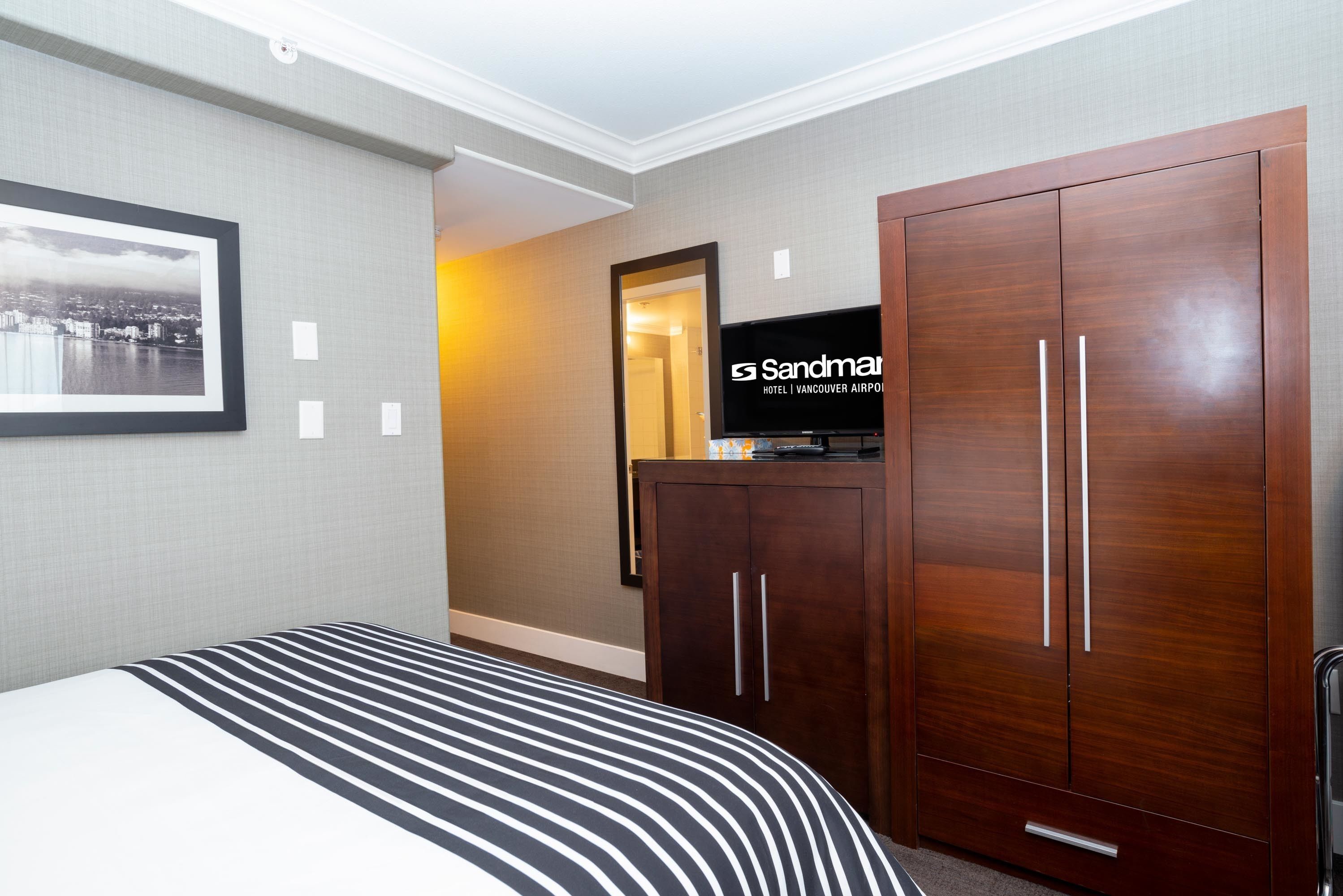 Una habitación de hotel con una cama grande, un armario, un televisor y un cuadro en la pared.