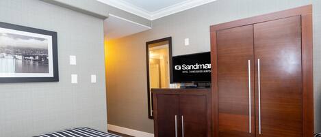Una habitación de hotel con una cama grande, un armario, un televisor y un cuadro en la pared.