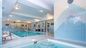 Une piscine intérieure avec des lignes de démarcation bien visibles, un poste de surveillance pour le sauveteur et une horloge au mur.