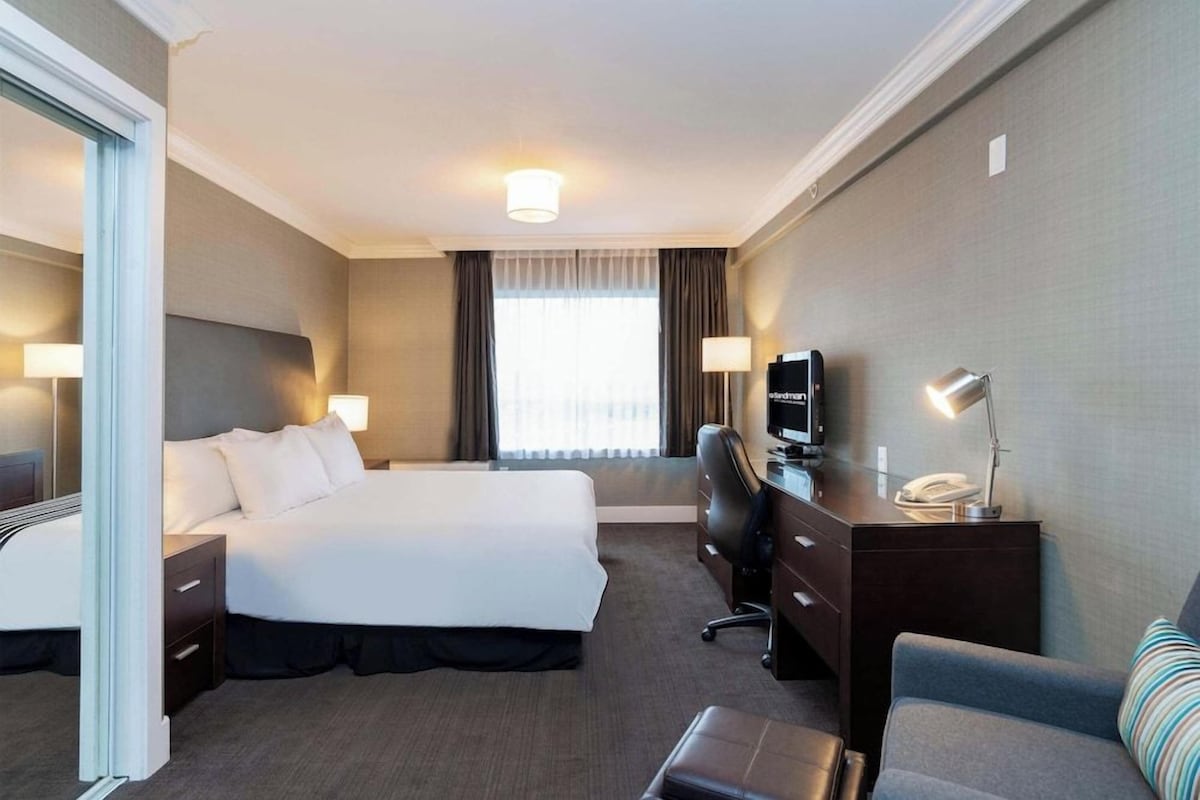 A hotel room with a bed, a desk with a computer, a chair, a lamp, and a television.