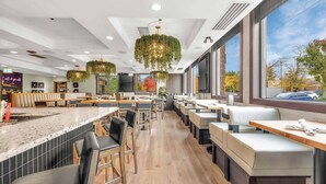 Een modern restaurant met een lange balie, meerdere zithoeken en grote ramen met uitzicht op buiten.