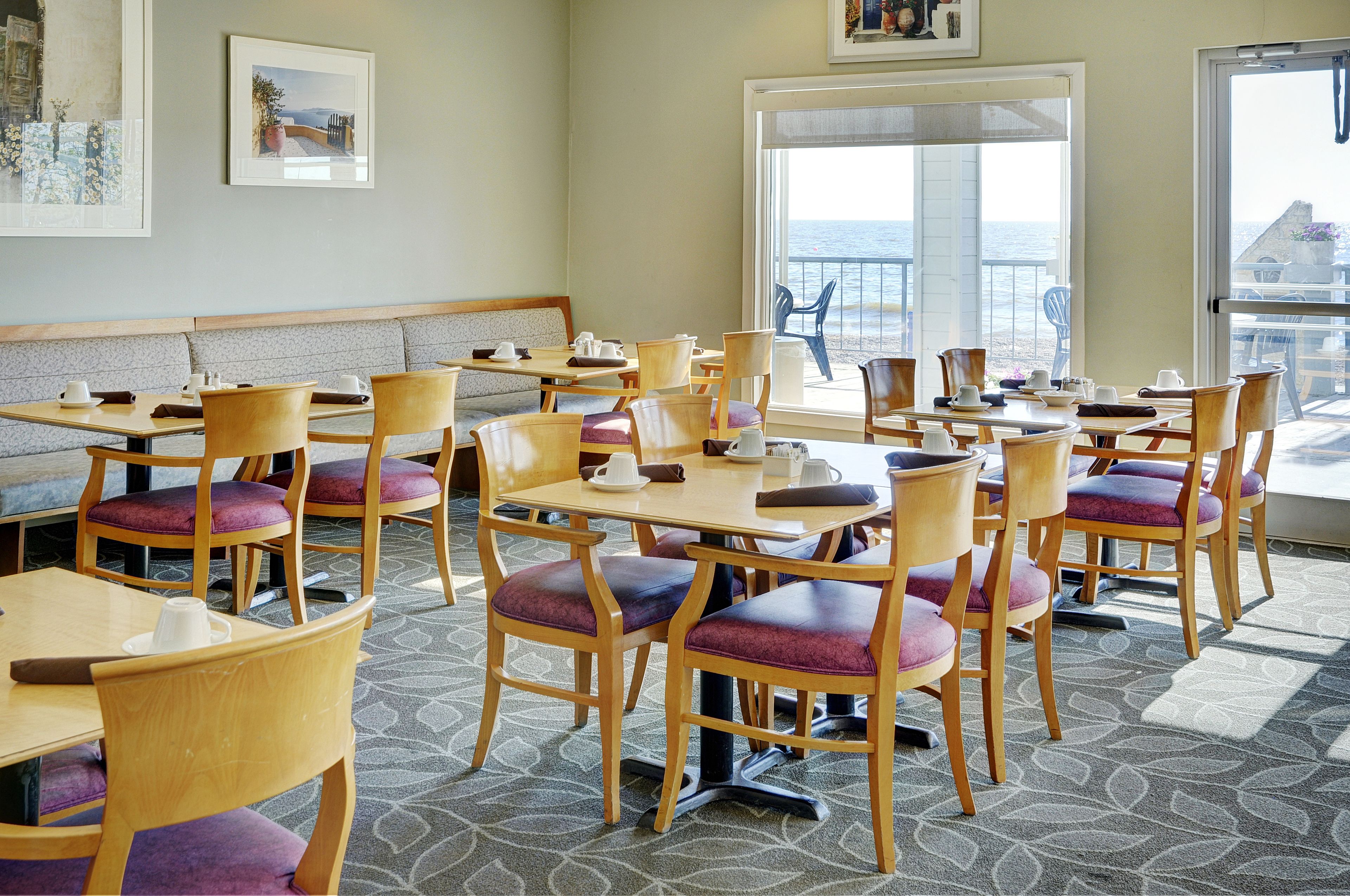 Un restaurante con mesas y sillas de madera, un banco y vista al mar.