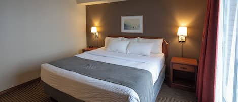 A hotel room with a large bed, two bedside tables with lamps, a framed picture on the wall, and a window with curtains.
