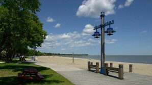A wooden boardwalk leading to a beach with picnic tables and benches, a lamp post, and a clear view of the ocean.