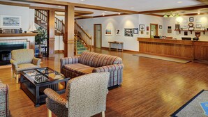 A spacious lobby with a fireplace, multiple seating areas, a reception desk, and a staircase.