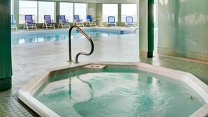 An indoor swimming pool with a hot tub, lounge chairs, and large windows.