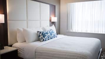 Una habitación de hotel con una cama grande, una mesita de noche, una lámpara de pared y una ventana con cortinas translúcidas.