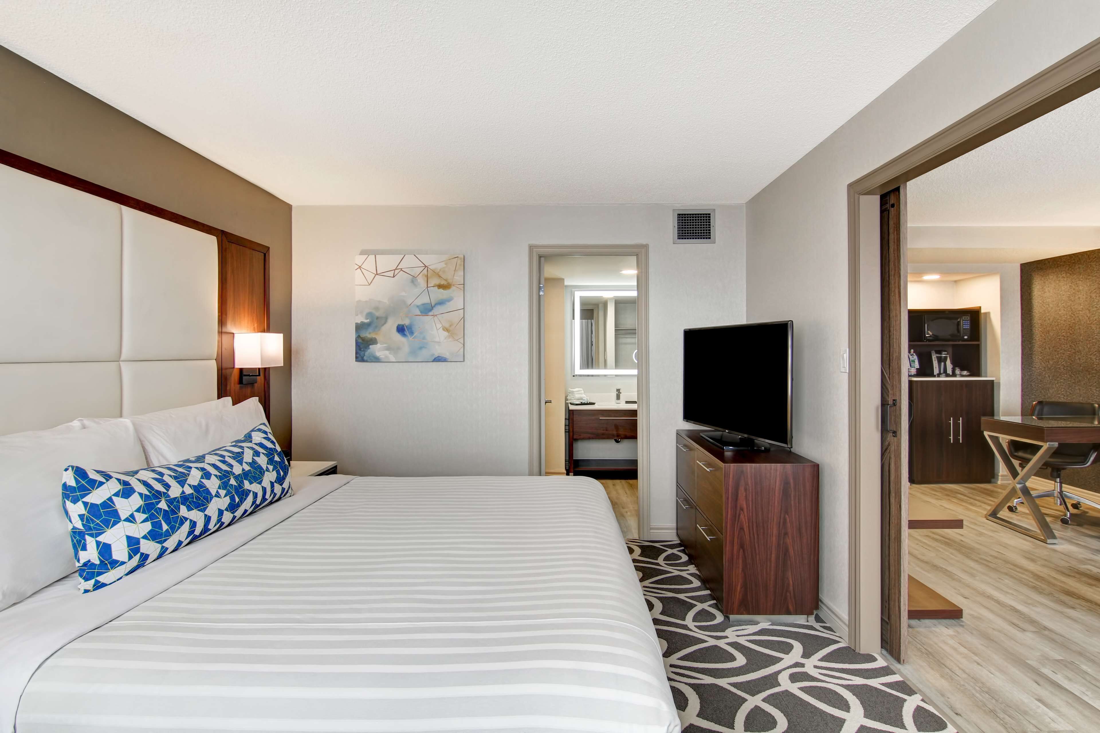 A hotel room with a large bed, a TV, a desk, and a bathroom visible through an open door.