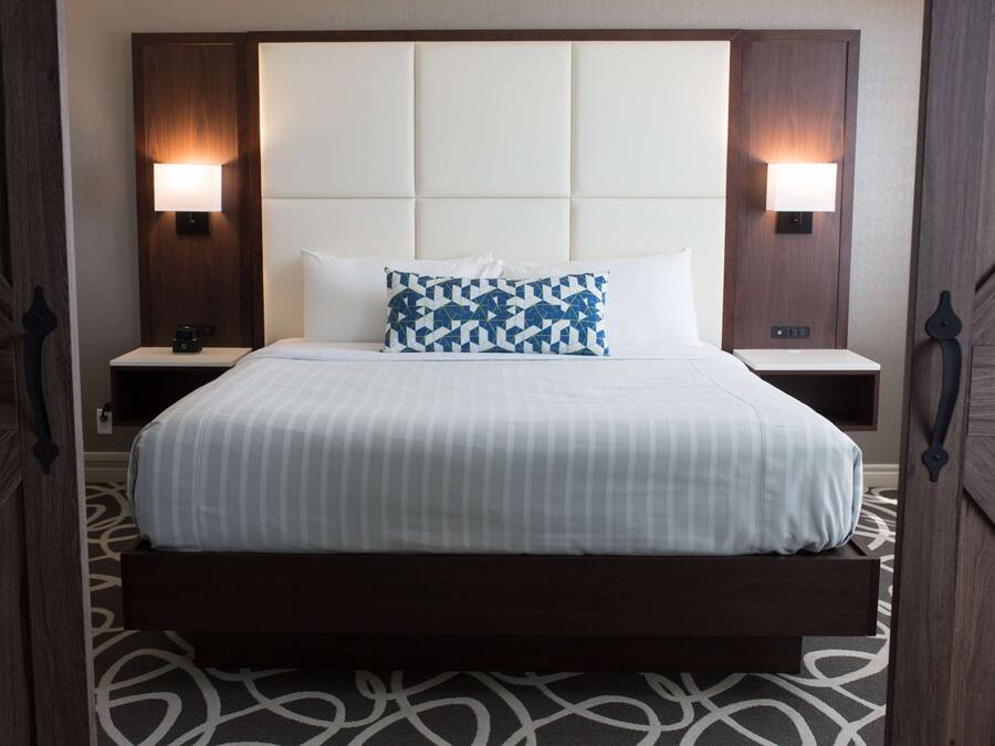 Quarto de hotel com uma cama grande, duas mesas de cabeceira e cabeceira com iluminação embutida.