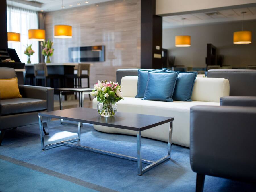 Un moderno hall de hotel con sofá, sillones, una mesa de centro e iluminación colgante.