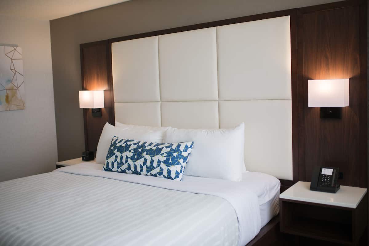 A hotel room with a large bed, a headboard with a padded back, two bedside lamps, a bedside phone, and a small table.