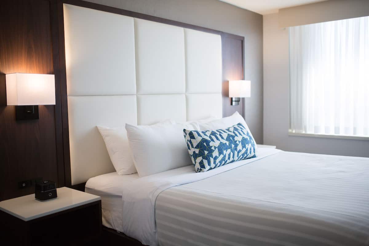 A hotel room with a large bed, two bedside lamps, a nightstand with a phone, and a window with curtains.