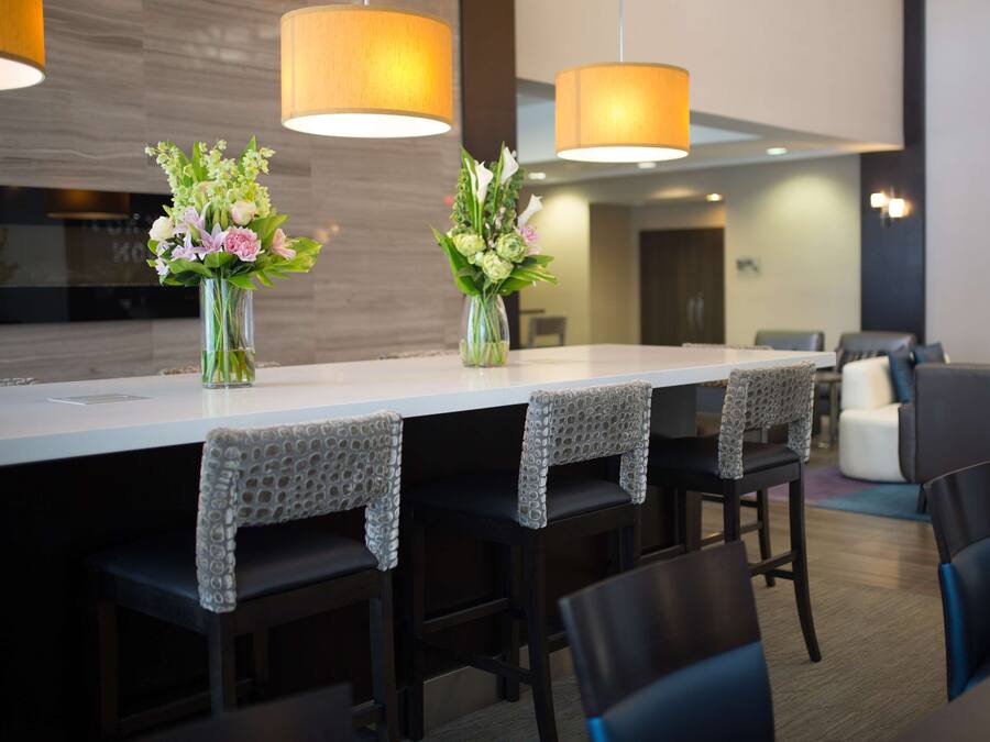 A modern dining area with a long table, dark chairs, and two vases of flowers.