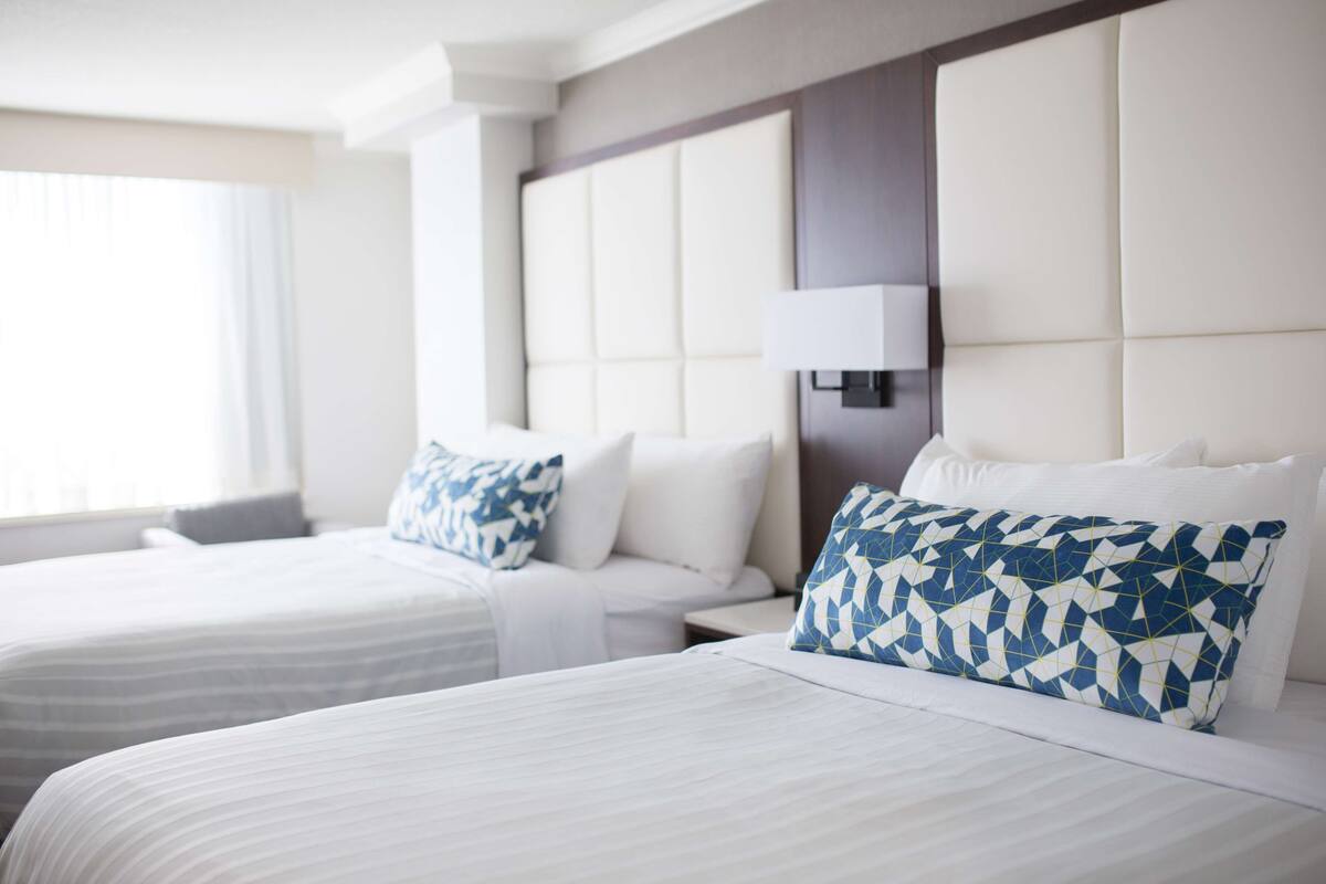 A hotel room with two beds, a large padded headboard, and a bedside table with a lamp.