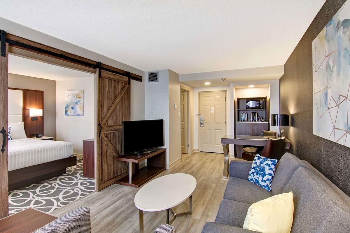 A hotel room with a bed, TV, sofa, dining table, and kitchenette.