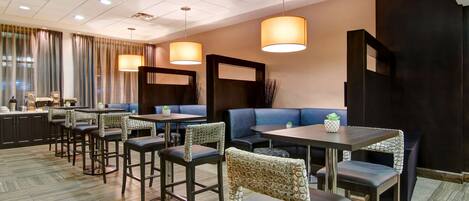 Un hall d’hôtel moderne doté de plusieurs espaces de détente, notamment des tabourets de bar et des tables, ainsi qu’un comptoir d’accueil.