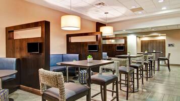 A hotel lobby with seating areas, tables, and a television screen.