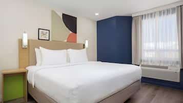 Un lit bien fait dans une chambre d’hôtel, avec une tête de lit, des tables de chevet et une fenêtre avec des rideaux.