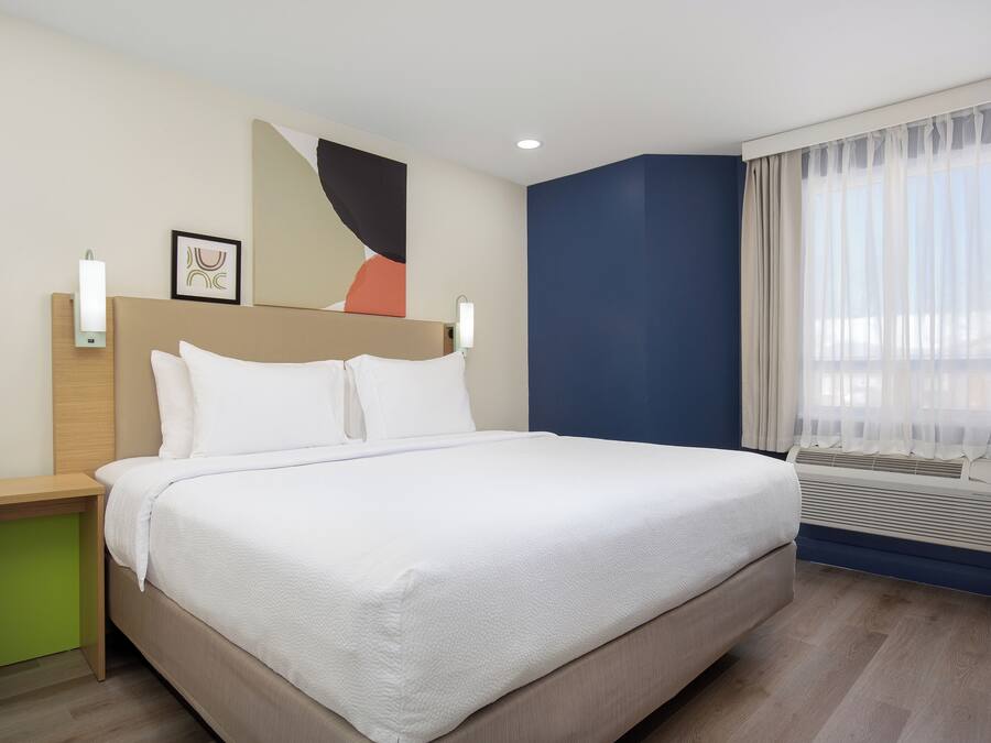 Un lit bien fait dans une chambre d’hôtel, avec une tête de lit, des tables de chevet et une fenêtre avec des rideaux.