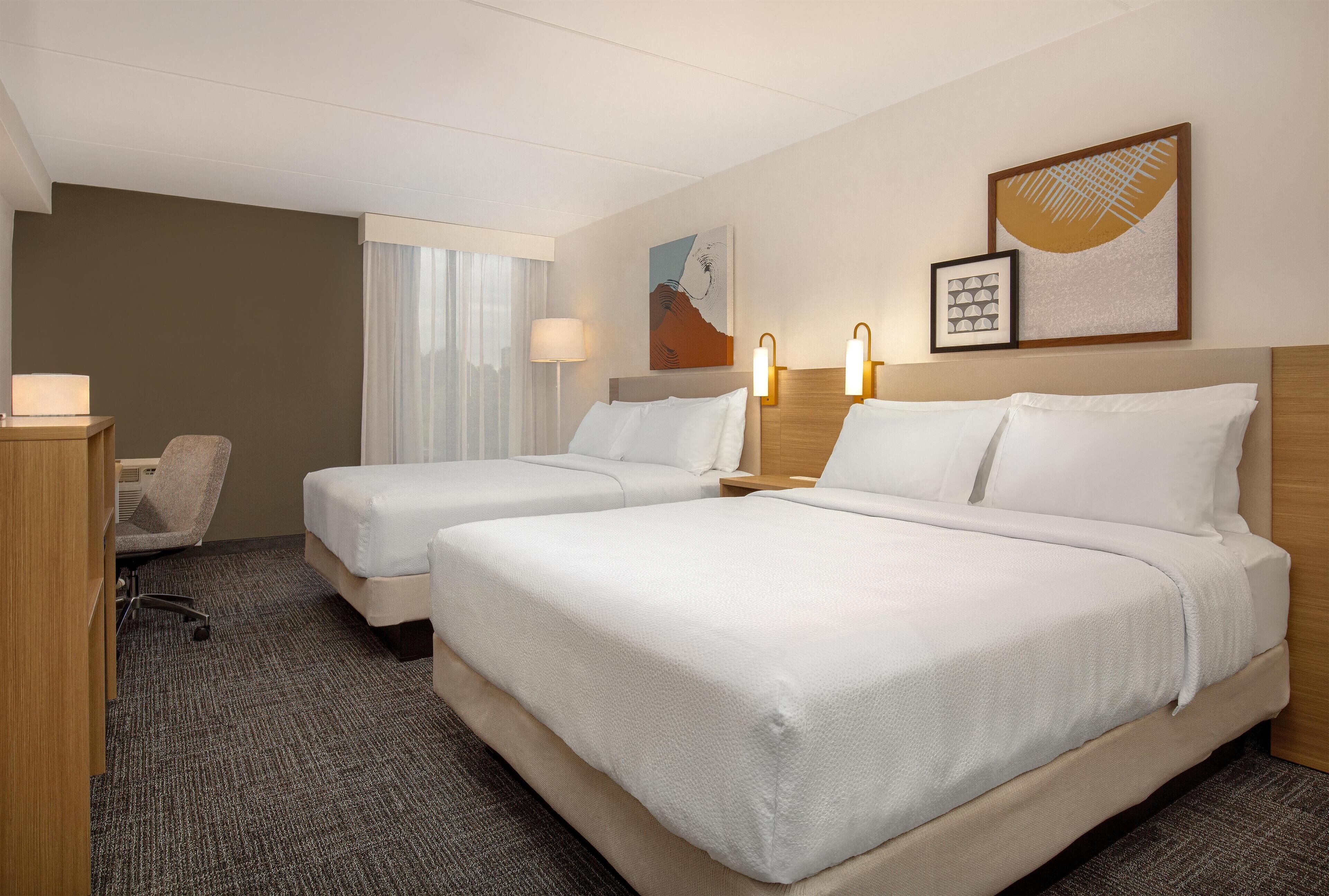 Een hotelkamer met twee bedden, een bureau, een stoel en een raam met gordijnen.