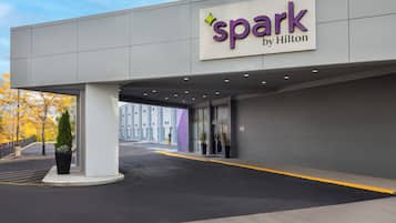 Een hotelingang met een 'spark by Hilton' bord, een overdekte doorgang en een parkeerplaats.