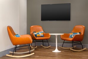 Una habitación con dos mecedoras naranjas, una mesa blanca y un televisor de pantalla plana montado en la pared.