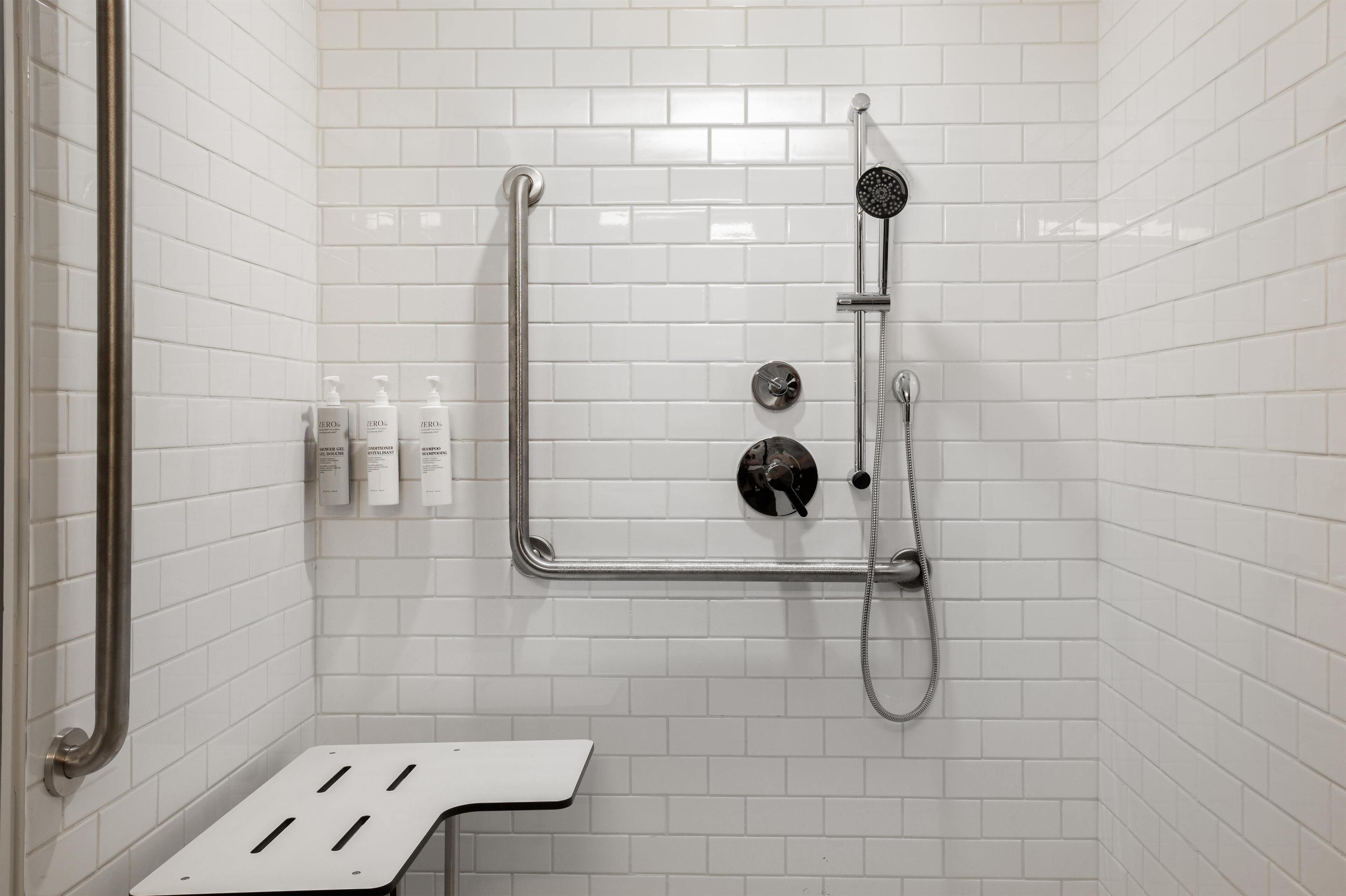 A white-tiled shower area with a handheld showerhead, a handheld shower attachment, and a handheld shower control.