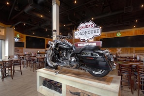 Interno di un ristorante con una moto esposta, tavoli e sedie in legno.