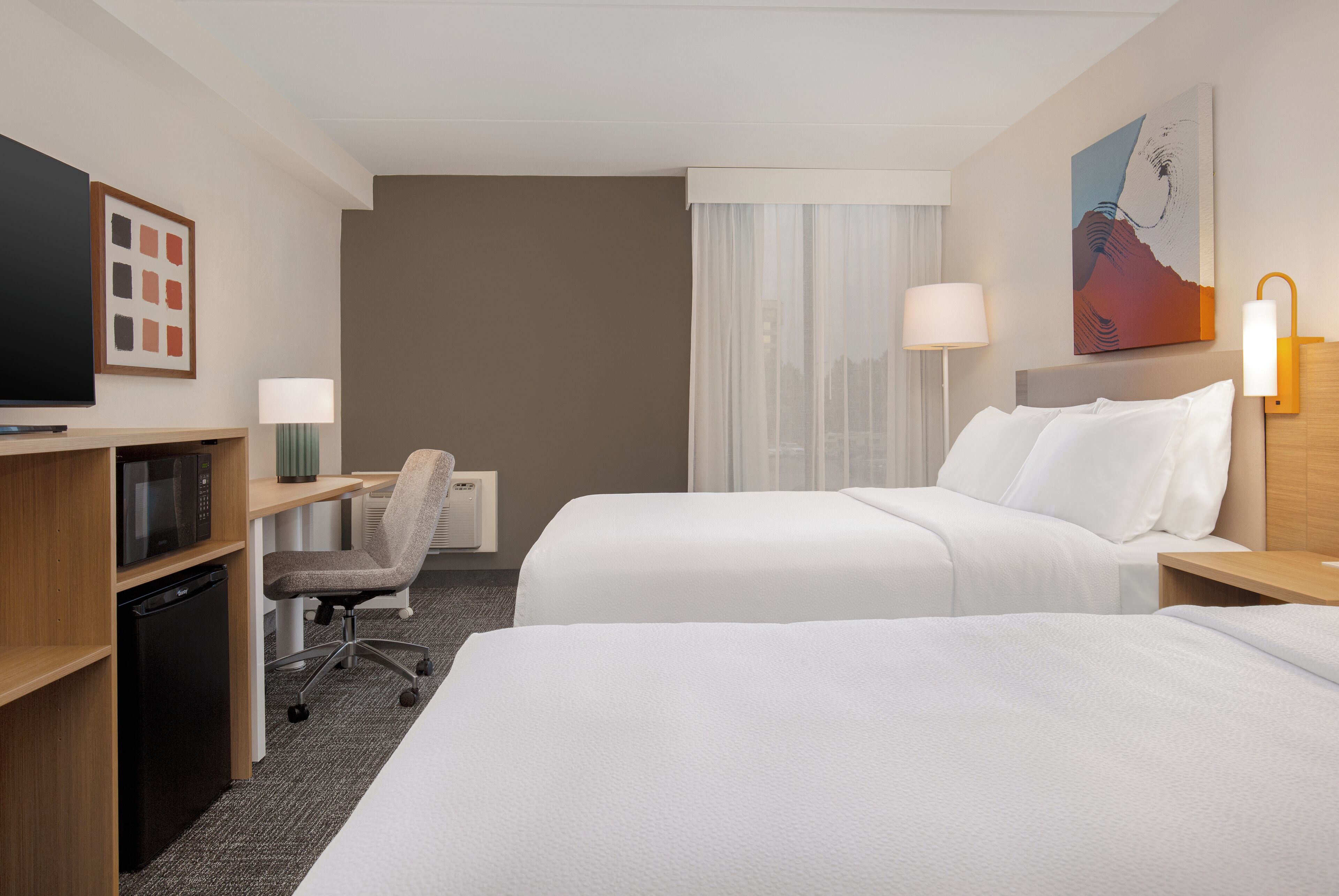 Ett hotellrum med två sängar, ett skrivbord med en stol, en tv och en mikrovågsugn.
