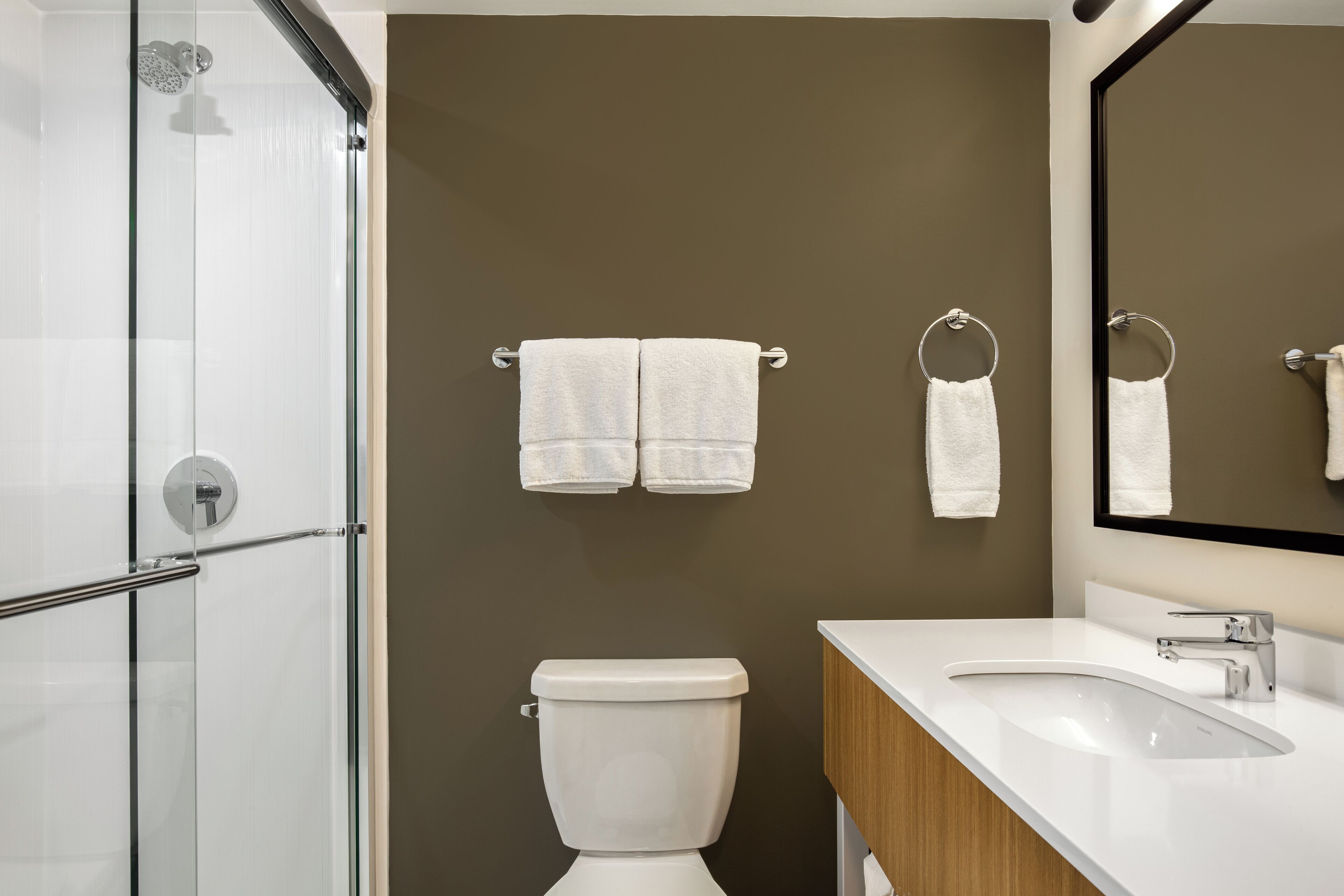 Un baño moderno con cabina de ducha de vidrio, inodoro blanco y lavamanos con tocador de madera.