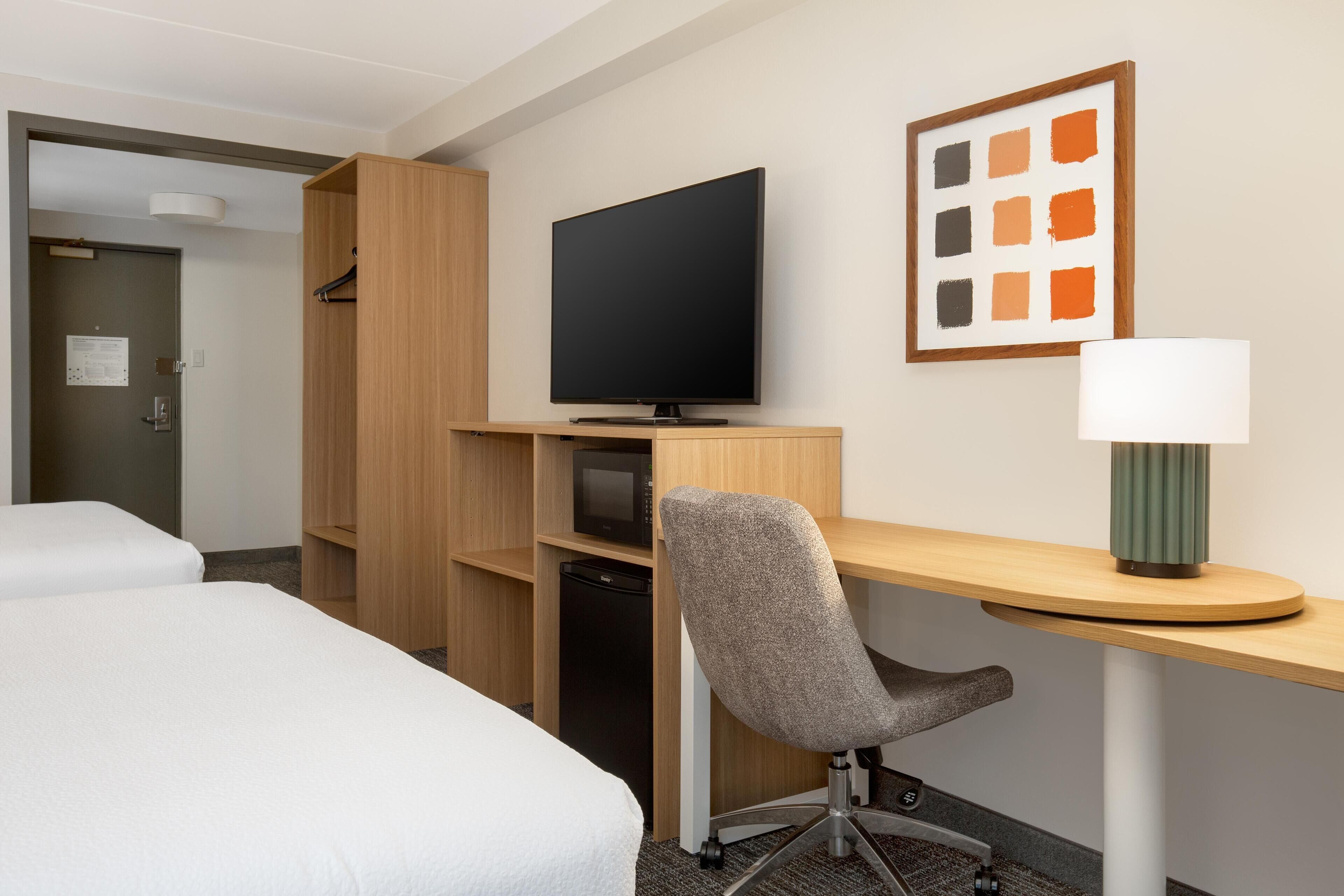 A hotel room with a bed, a desk with a chair, a television, a microwave, and a refrigerator.