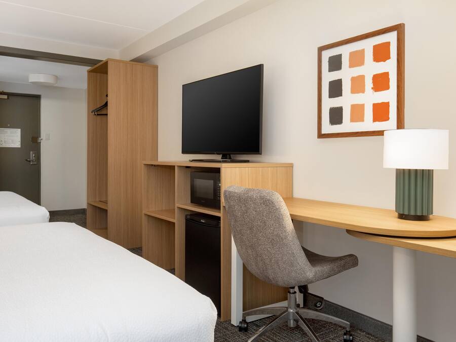A hotel room with a bed, a desk with a chair, a television, a microwave, and a refrigerator.