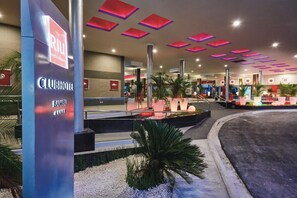 A Clubhotel Bambu with a modern entrance, palm trees, and a well-lit lobby area.