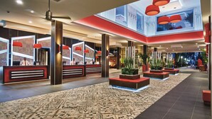 A spacious lobby with a high ceiling, red pendant lighting, and a patterned carpet.