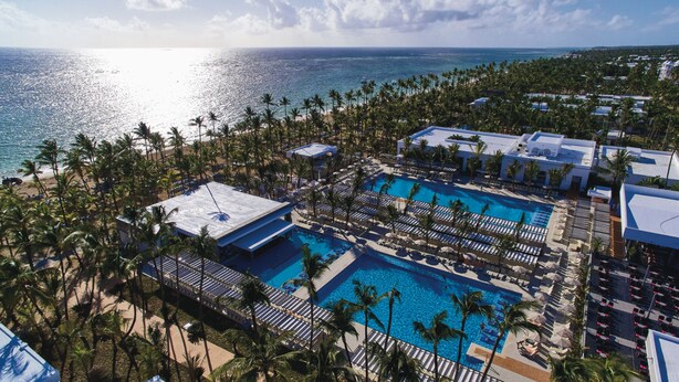 An aerial view of a resort with multiple swimming pools surrounded by palm trees and beach access.