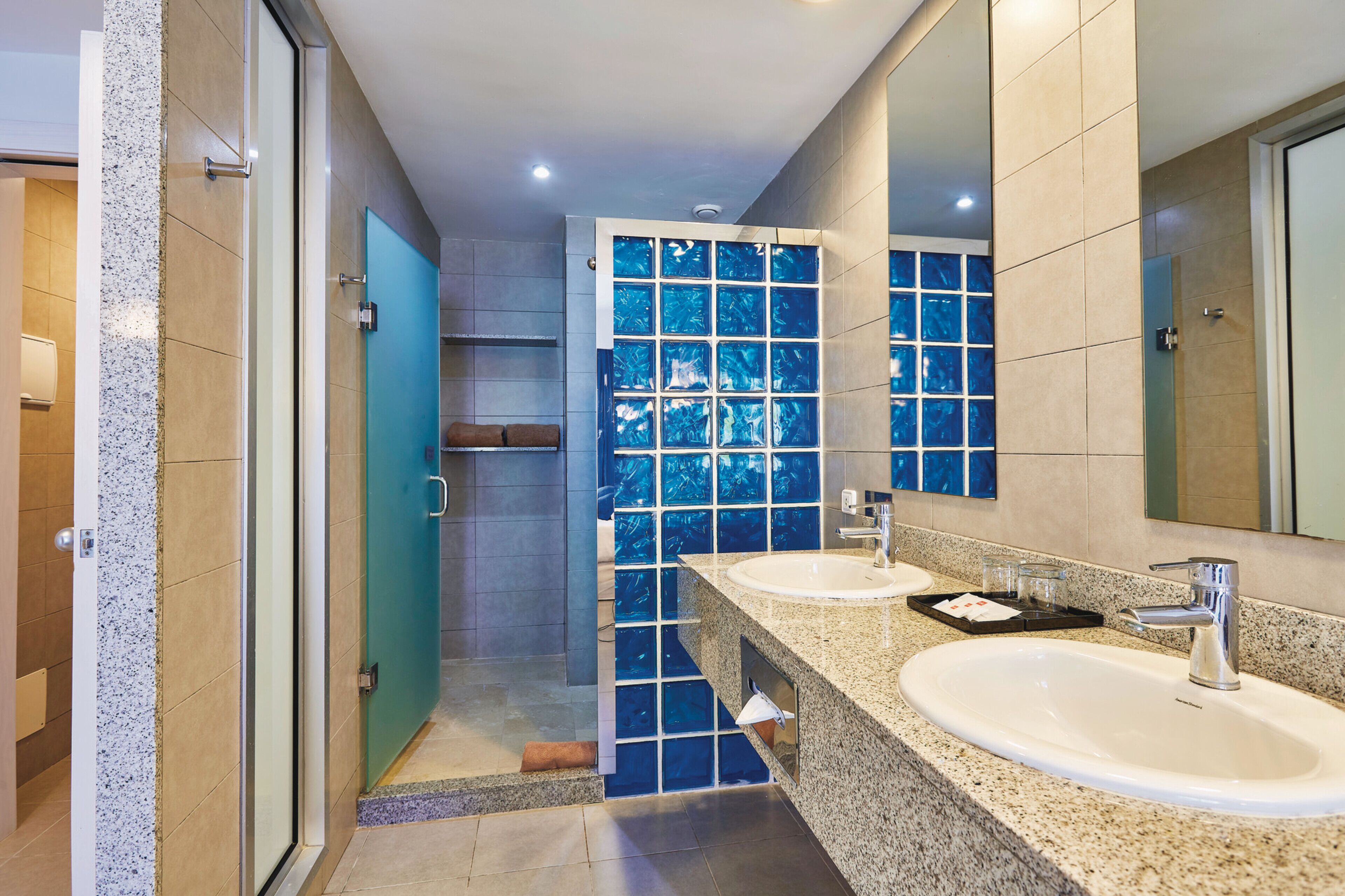 Une salle de bain moderne avec deux lavabos, une douche à l’italienne en verre et un grand miroir.