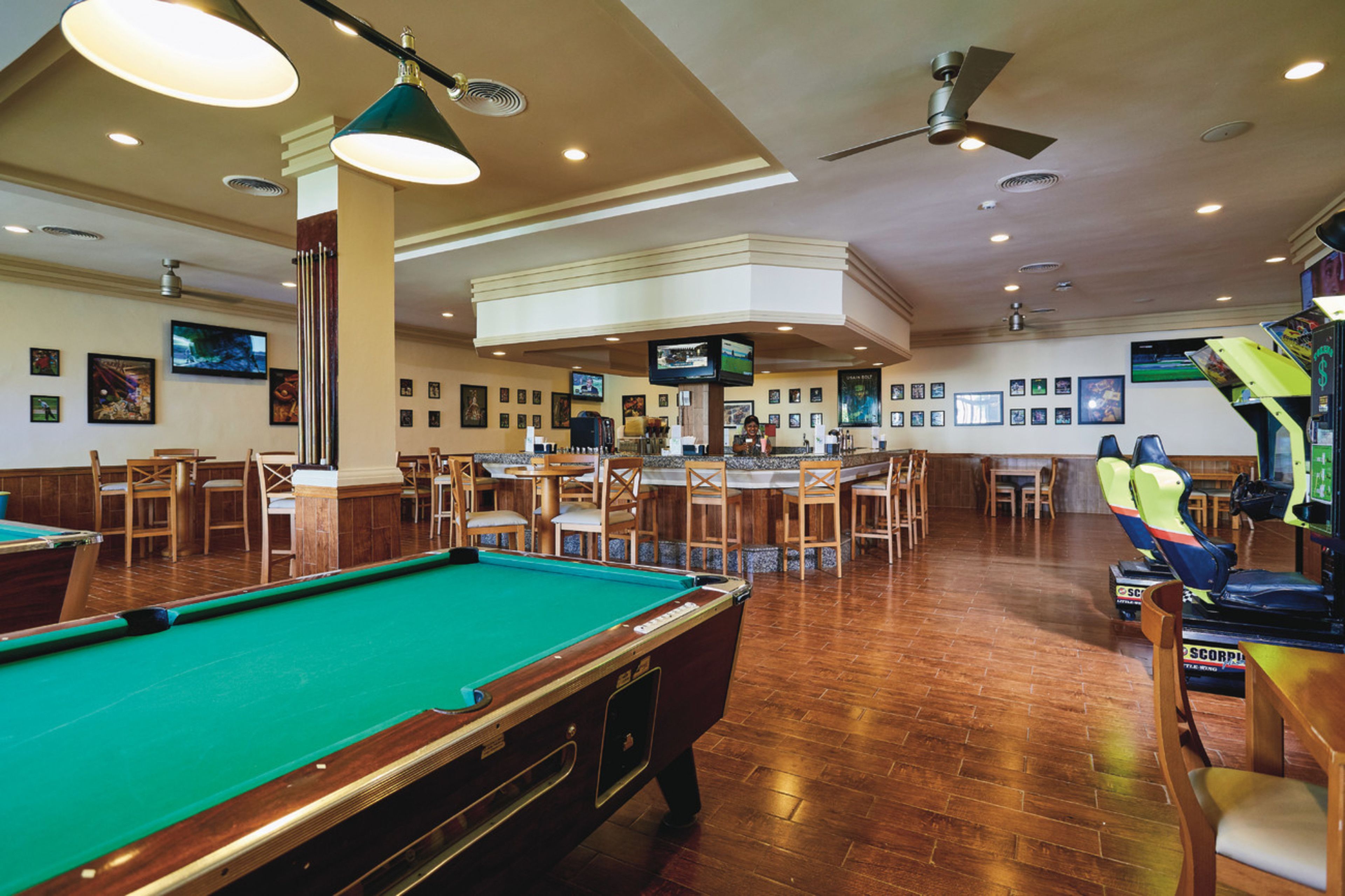 A pool table in a room with multiple seating areas, ceiling fans, and wall-mounted televisions.