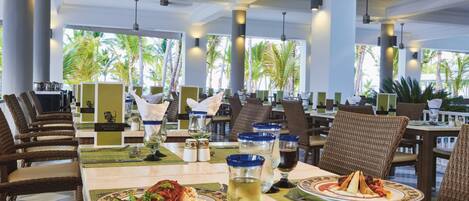 A restaurant with tables set for dining, featuring a view of palm trees outside.