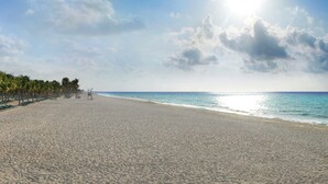 A beach with a clear sky, palm trees, and a lifeguard tower.