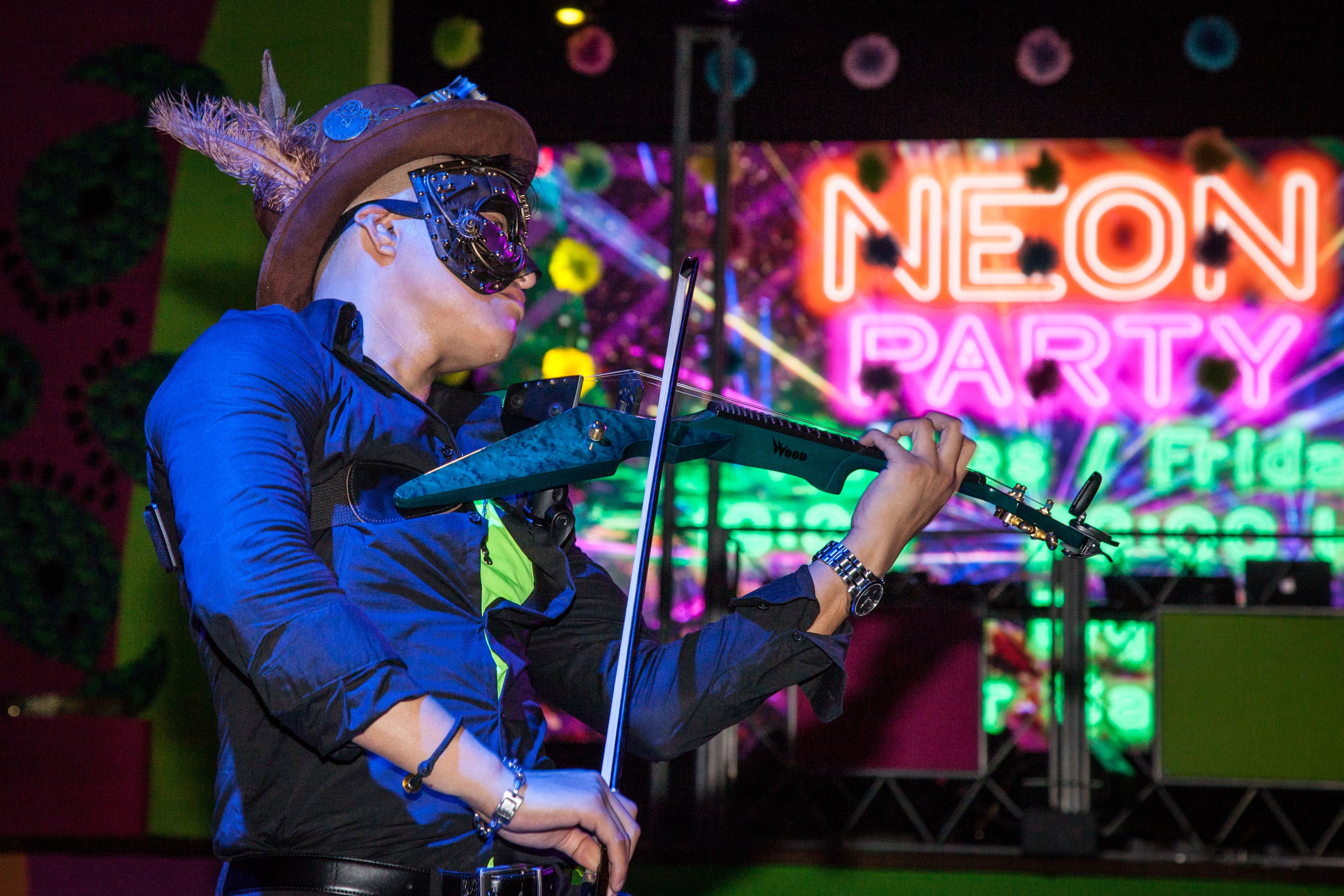 A person playing a guitar on a stage with a neon sign in the background that reads "NEON PARTY".