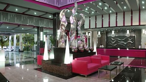 A modern lobby with a reception desk, a seating area with pink sofas, and a decorative water feature.