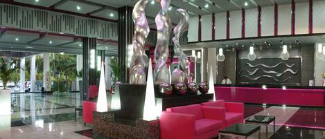 Un hall d’entrée moderne comprenant un comptoir d’accueil, un espace salon avec des canapés roses et un élément décoratif aquatique.