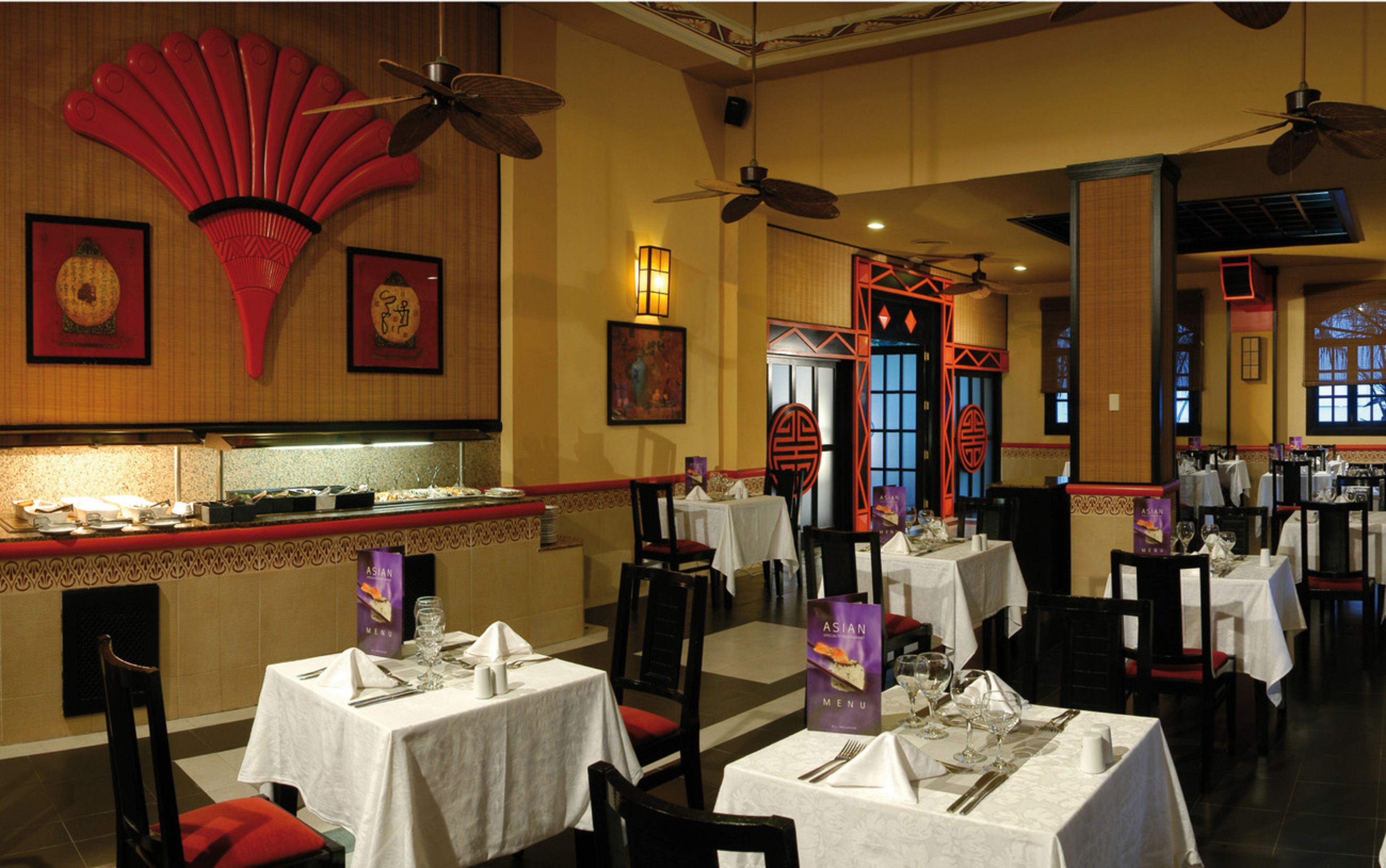 Un restaurante con varias mesas, ventiladores de techo y decoración asiática tradicional.