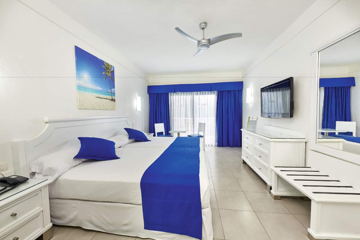 A hotel room with a large bed, a TV, a desk, and a window with curtains.