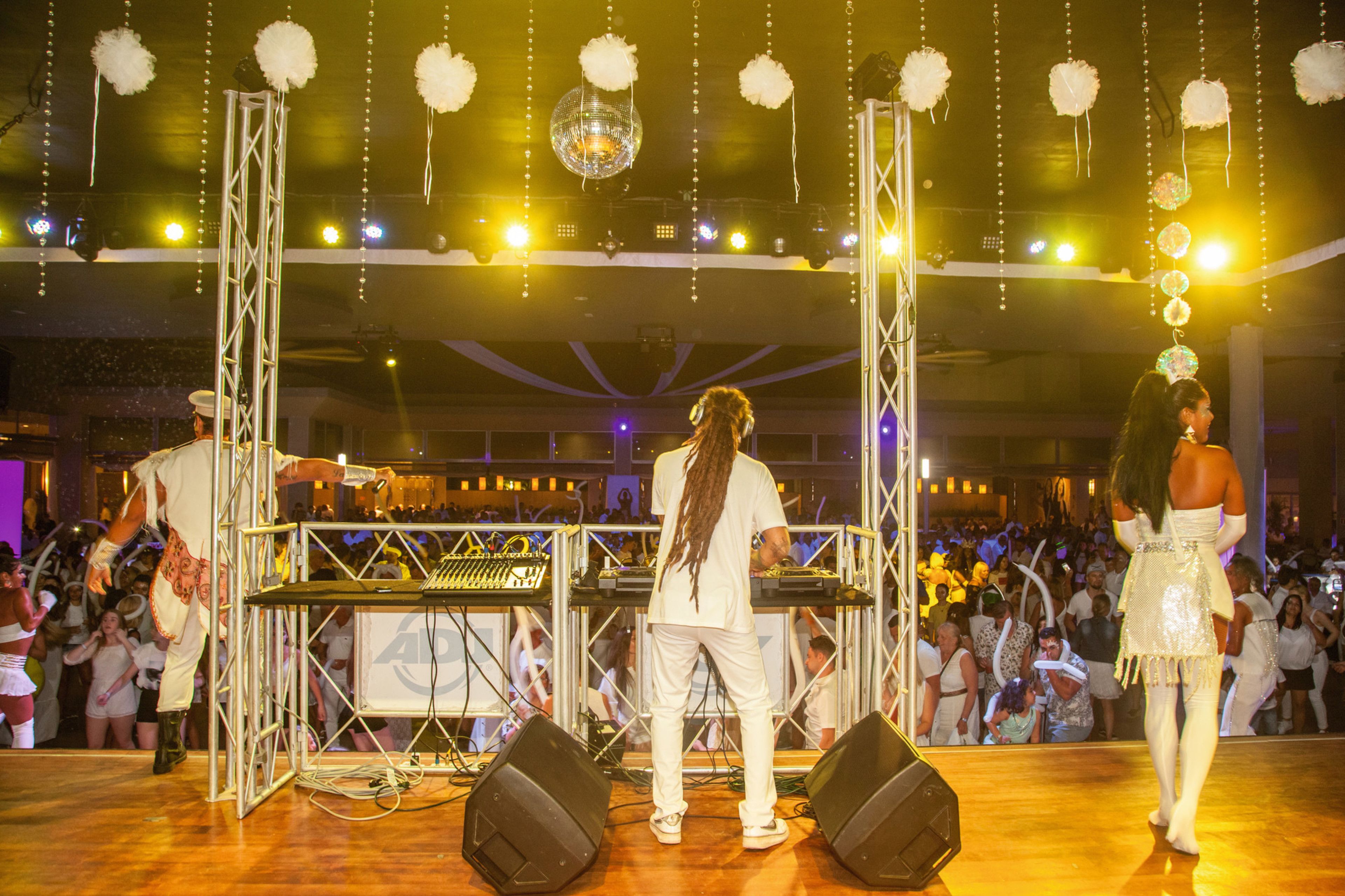 A stage with a DJ setup, a crowd of people, and a decorative chandelier.