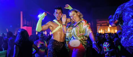 Evento interior concurrido donde personas bailan y conversan.