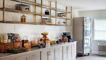 A kitchen with white cabinets, a stainless steel refrigerator, and a bamboo shelf unit with storage containers.
