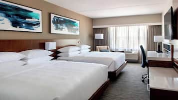 A hotel room with two beds, a desk, a chair, a TV, and artwork on the walls.